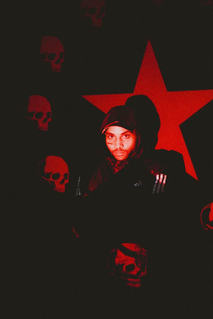 Photo de presse du rappeur 8ruki devant le drapeau composé d'une étoile et de crânes rouges sur un fond noir représentant la cover de sa mixtape "POURquoi!!" sorti le 19 janvier 2024.